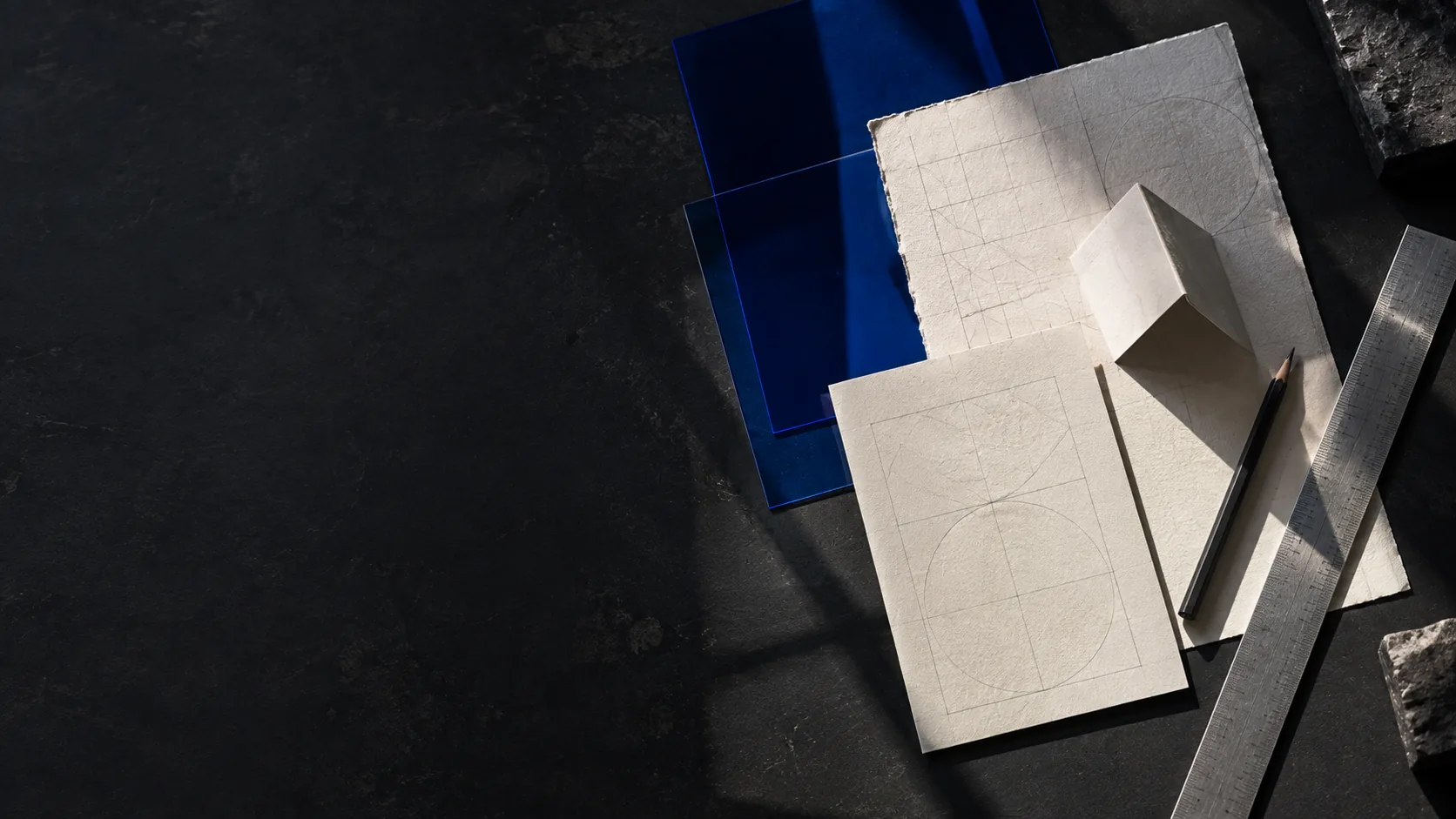 Gestaltungsmaterialien auf einem dunklen Arbeitstisch: Papier, kobaltblaue Folien und Zeichenwerkzeuge
